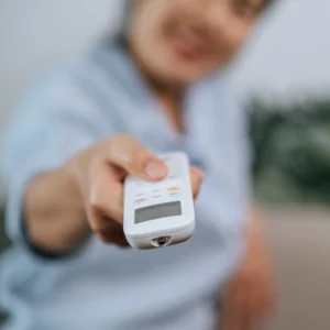 Hand holding AeroChill air conditioner remote control for smart Wi-Fi operation.